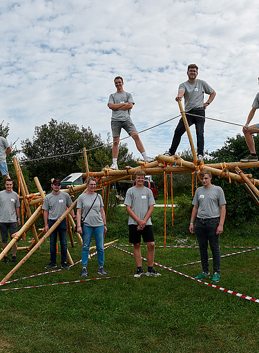 Foto von vielen jungen Auszubildenden, die aus Holz eine Brücke gebaut haben