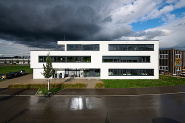 Foto des Gebäudes von der Straße aus mit Regenwolken