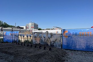 Baufeld mit Bauzaunbanner sowie Spaten und Bauhelme
