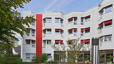 Foto Gebäude mit roten Elementen in der Fassade und rotem Sonnenschutz