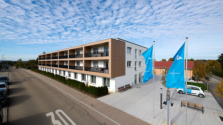 Foto von außen entlang der Gebäudefront mit Fahnen