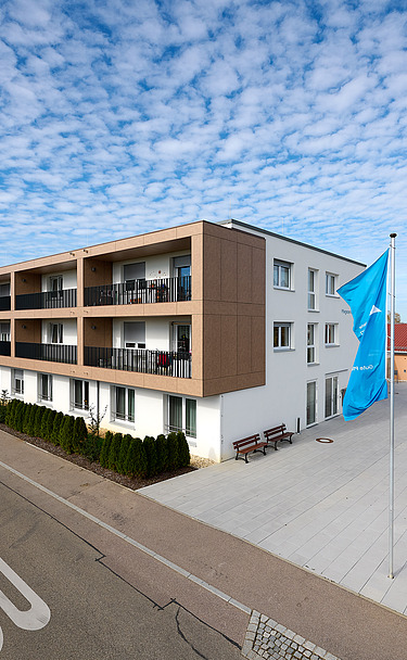 Foto von außen entlang der Gebäudefront mit Fahnen