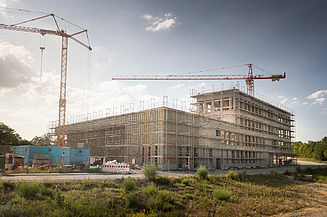 Foto von einem Gebäude, das sich im Bau befindet sowie 2 Kräne