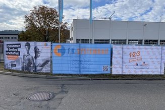 Zaun mit Bannern, im Hintergrund Werkstattgebäude