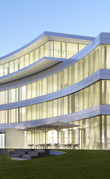 Foto Gebäude mit beleuchteten Fenstern in Abendstimmung. Markantes, überstehendes Dachgeschoss