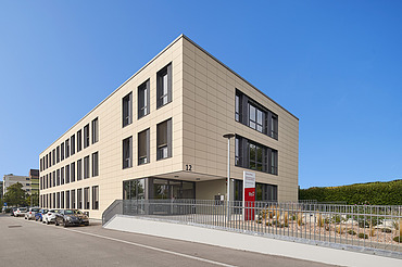 Foto von Gebäude von weiter weg mit Straße, Eingang und blauem Himmel