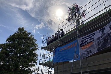 eingerüstetes Gebäude mit Richtbaum und Zimmermannsleuten