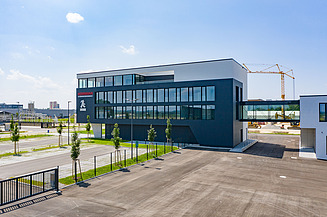 Foto von Gebäude mit dunkler Fassade mit Parkplatz und Verbindungsbrücke zu Lagerhalle