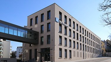 Foto auf ein Gebäudeteil mit Verbindungssteg aus Glas zum nächsten Gebäudeteil