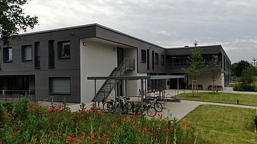 Foto von Gebäudeecke und Fahrradstellplatz mit Blumenwiese