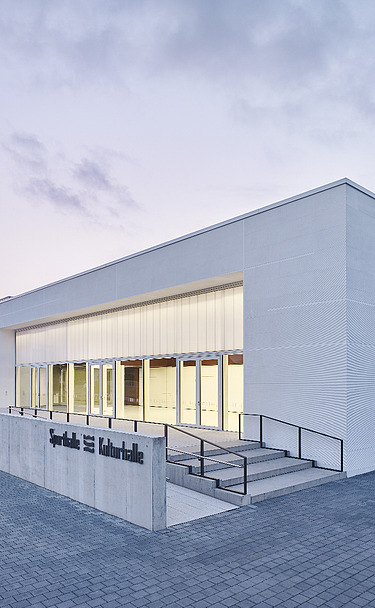 Foto Eckansicht Sporthalle mit gepflastertem Weg und Eingang