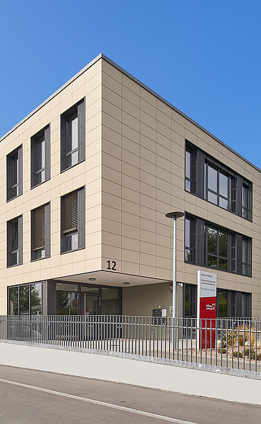 Foto von Gebäude von weiter weg mit Straße, Eingang und blauem Himmel