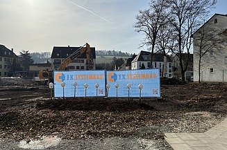 Baufeld mit Bauzaunbanner sowie Spaten und Bauhelme