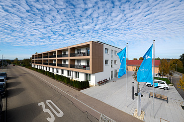 Foto von außen entlang der Gebäudefront mit Fahnen