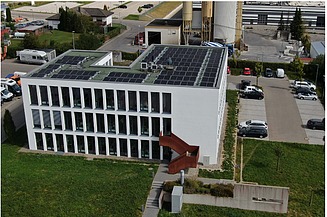 Hier sehen Sie eine Drohnenaufnahme unseres Firmengebäudes. Der Fokus liegt auf der auf dem Dach montierten Photovoltaikanlage.