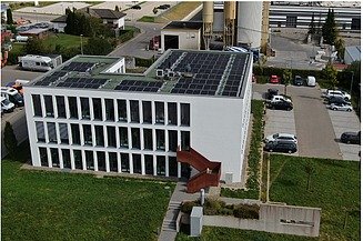 Hier sehen Sie eine Drohnenaufnahme unseres Firmengebäudes. Der Fokus liegt auf der auf dem Dach montierten Photovoltaikanlage.