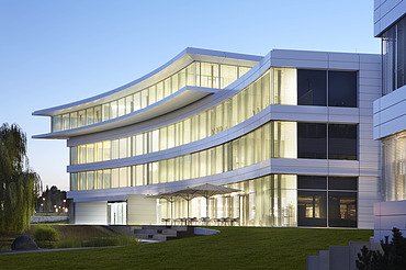 Foto Gebäude mit beleuchteten Fenstern in Abendstimmung. Markantes, überstehendes Dachgeschoss