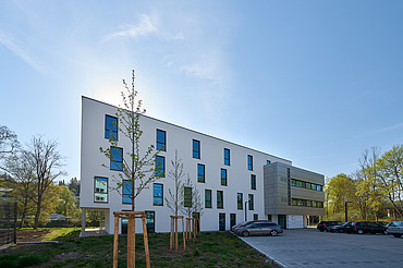 Foto von Gebäude von weiter weg mit Parkplatz und blauem Himmel