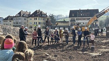 Erwachsene und Kinder, die mit einem Spaten Erde in die Luft werfen