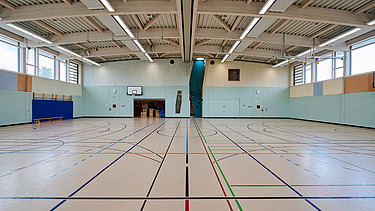 Foto im Inneren der Sporthalle mit Holzdecke, Kletterwand und Sportelementen