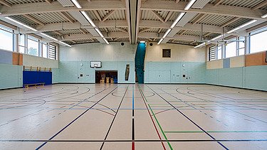 Foto im Inneren der Sporthalle mit Holzdecke, Kletterwand und Sportelementen