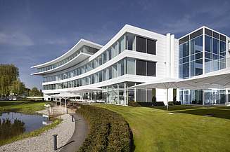 Foto von Gebäude mit weißer Fassade und Parkanlage mit See im Vordergrund