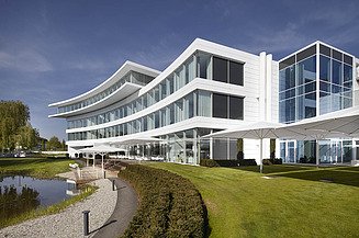 Foto von Gebäude mit weißer Fassade und Parkanlage mit See im Vordergrund