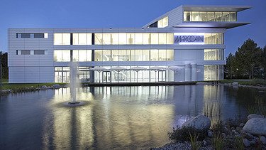 Foto beleuchtetes Gebäude in Abendstimmung mit See und Wasserfontänen im Vordergrund