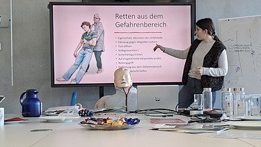 Eine Frau erklärt anhand eines Schaubild Rettung aus dem Gefahrenbereich