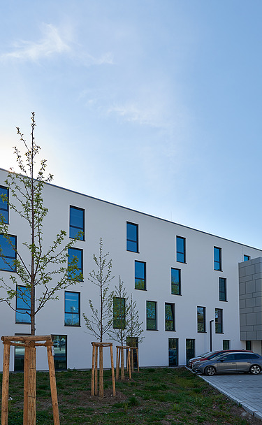 Foto von Gebäude von weiter weg mit Parkplatz und blauem Himmel