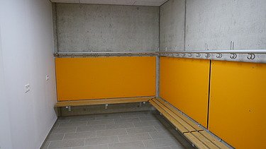 Innenaufnahme Umkleide mit Sichtbeton und orangenem Farbelement